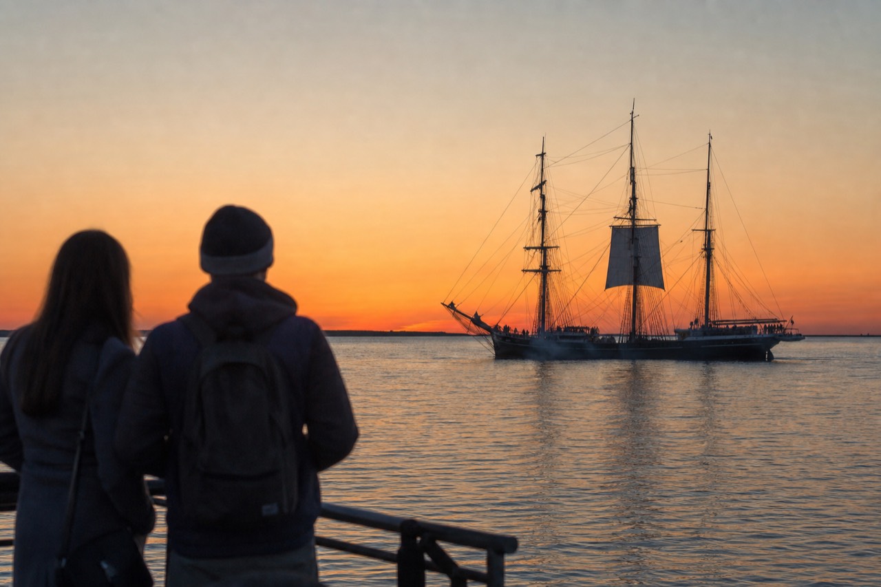 Tall ship silhouetted against an orange Key West sunset over calm water, no text, no logos, no people.