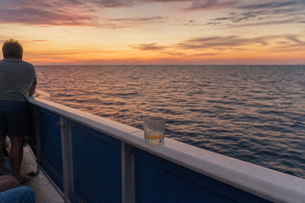Sunset over open Gulf water seen from a boat deck with railings and no land in view, no text, no logos, no people