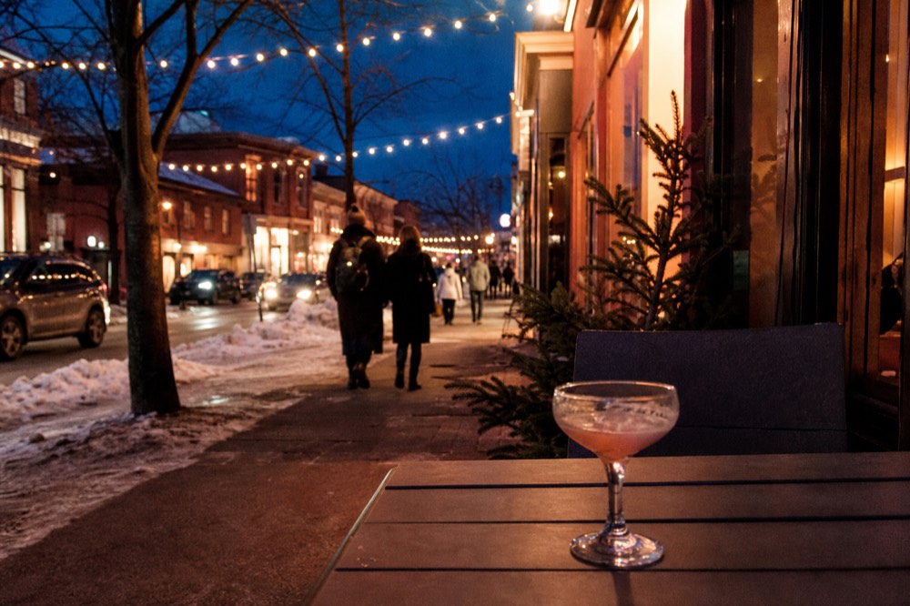 A lit-up street at dusk with people strolling past colorful storefronts, no text, no logos, no people