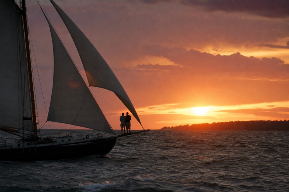 Schooner silhouetted against a fiery sunset, no text, no logos, no people