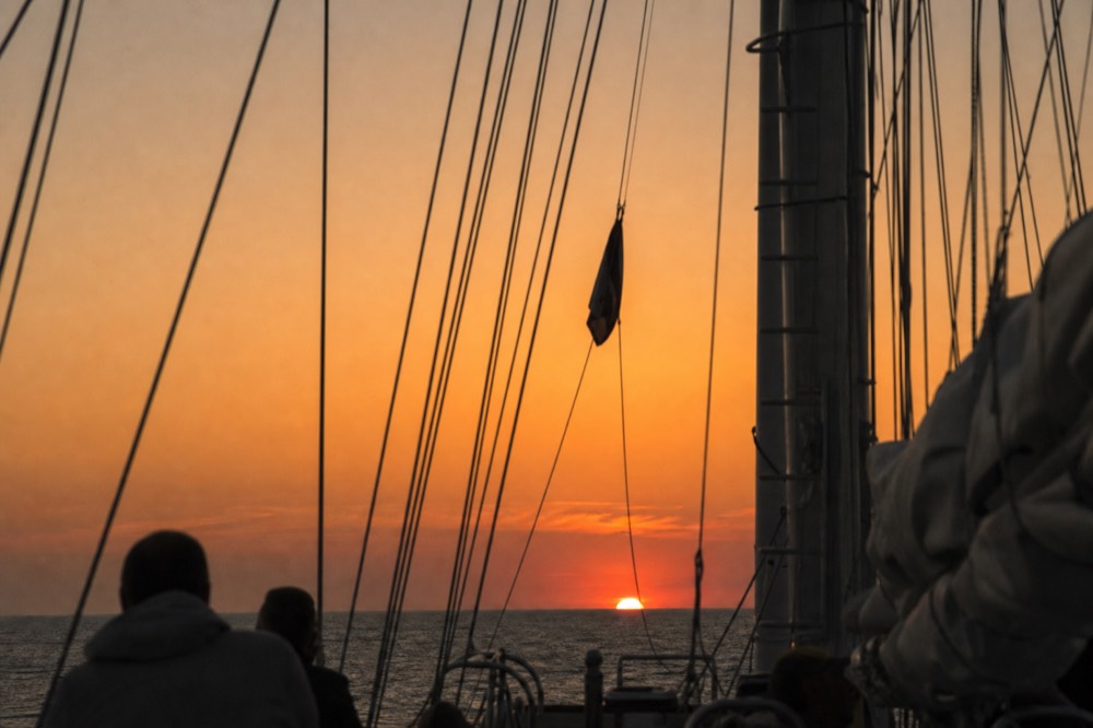 A schooner's rigging silhouetted against an orange Key West sunset sky, no text, no logos, no people
