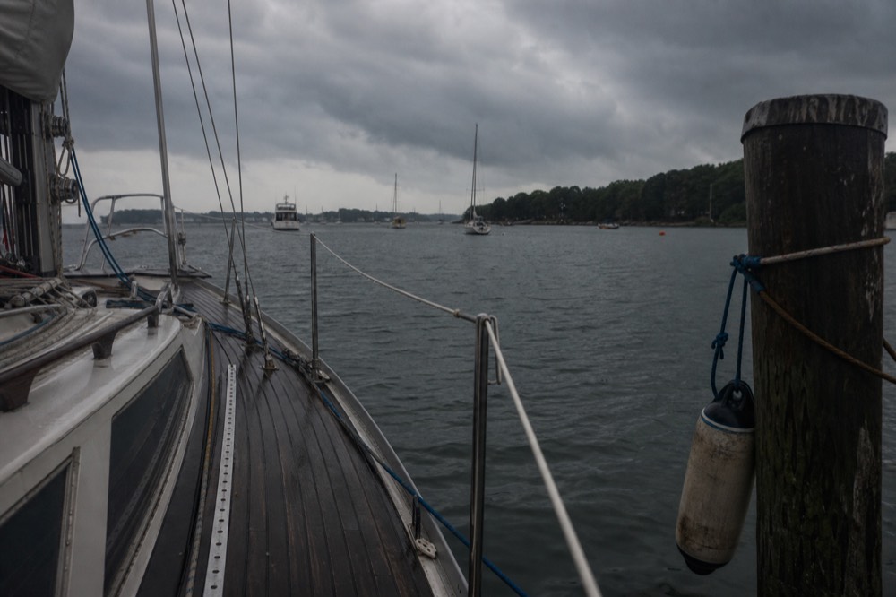 An empty deck of a moored sailboat under a cloudy grey evening sky, no text, no logos, no people.