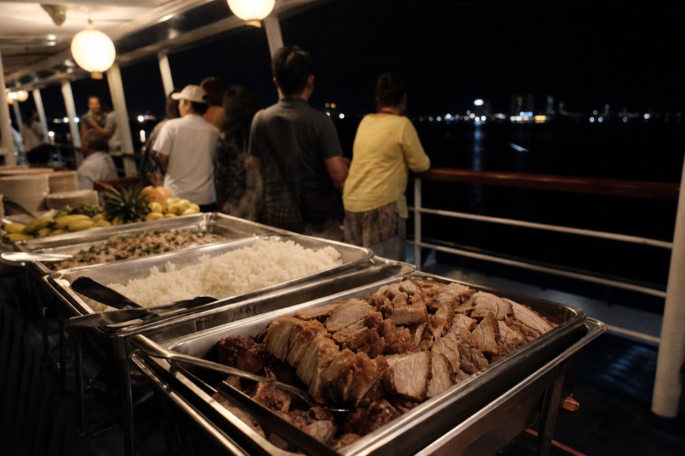 A serving table of tropical buffet dishes under lantern light on a boat, no text, no logos, no people.