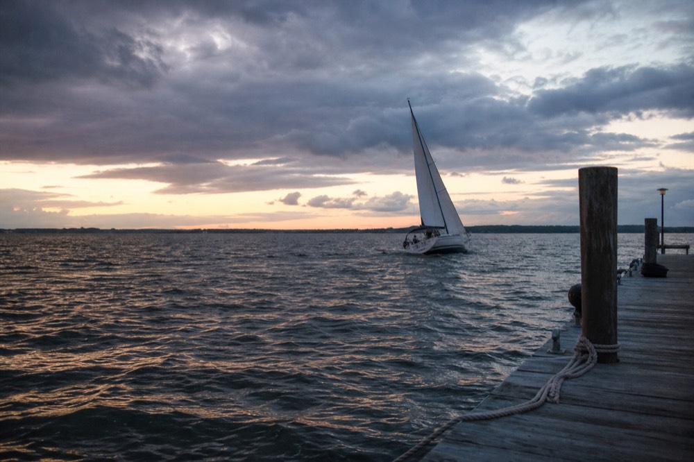 A boat under sail at sunset seen from a quiet dock, no text, no logos, no people.